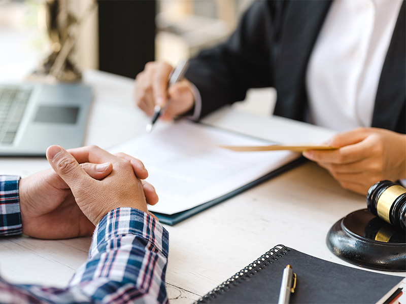 Anwältin und Gekündigter prüfen Arbeitsvertrag, mehrere Dokumente liegen aus — typisches Setting für anwaltliche Arbeitsrechtsberatung.