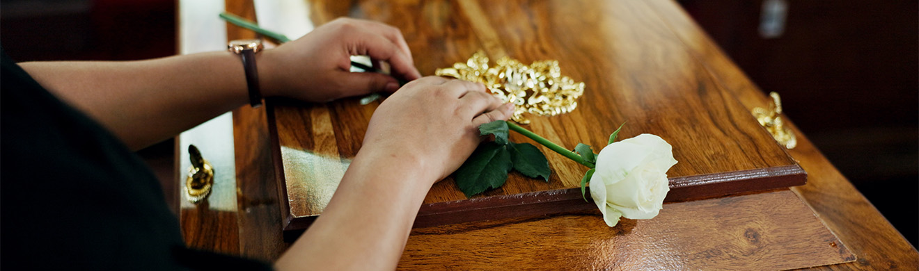 Hände legen eine Rose auf den Sarg während einer Erdbestattung in Herborn bei einer würdevollen Trauerfeier
