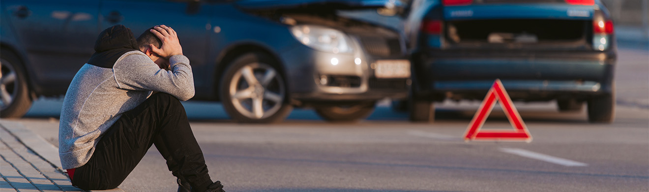 Trauriger Mann nach Autounfall auf Straße, symbolisch für rechtliche Probleme und Verkehrsrecht in Gießen.